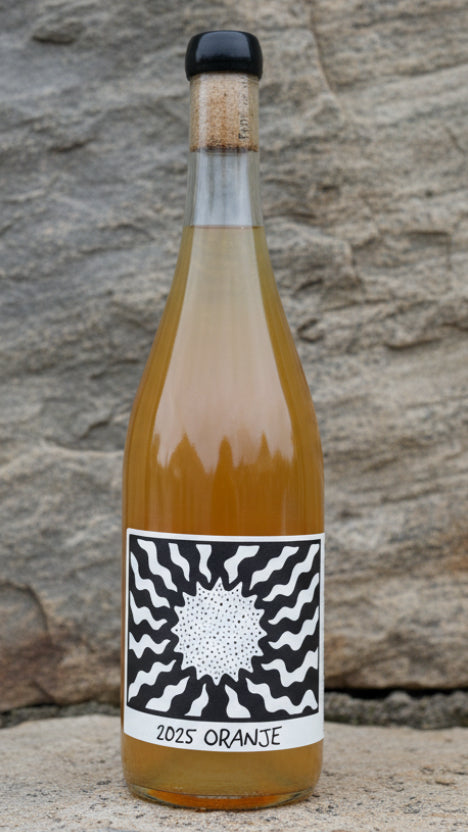 Bottle of 2025 Orange juice with a black and white label on a wooden surface.